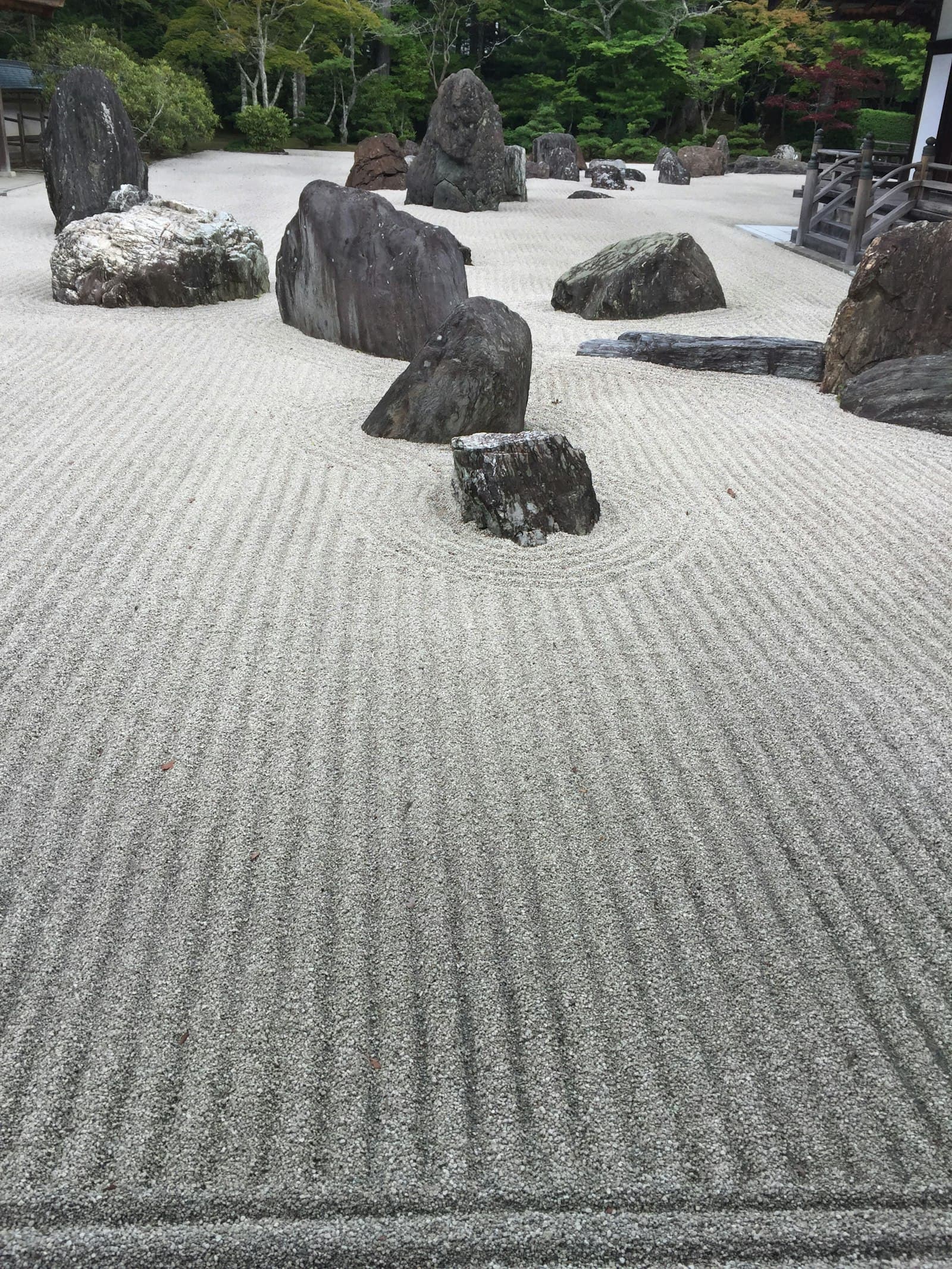 A raked gravel garden with weathered boulders and moss set against a wooded backdrop